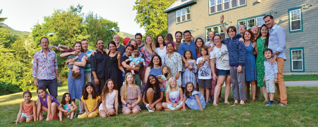 A big group of adults and kids pose in the backyard of a large house.